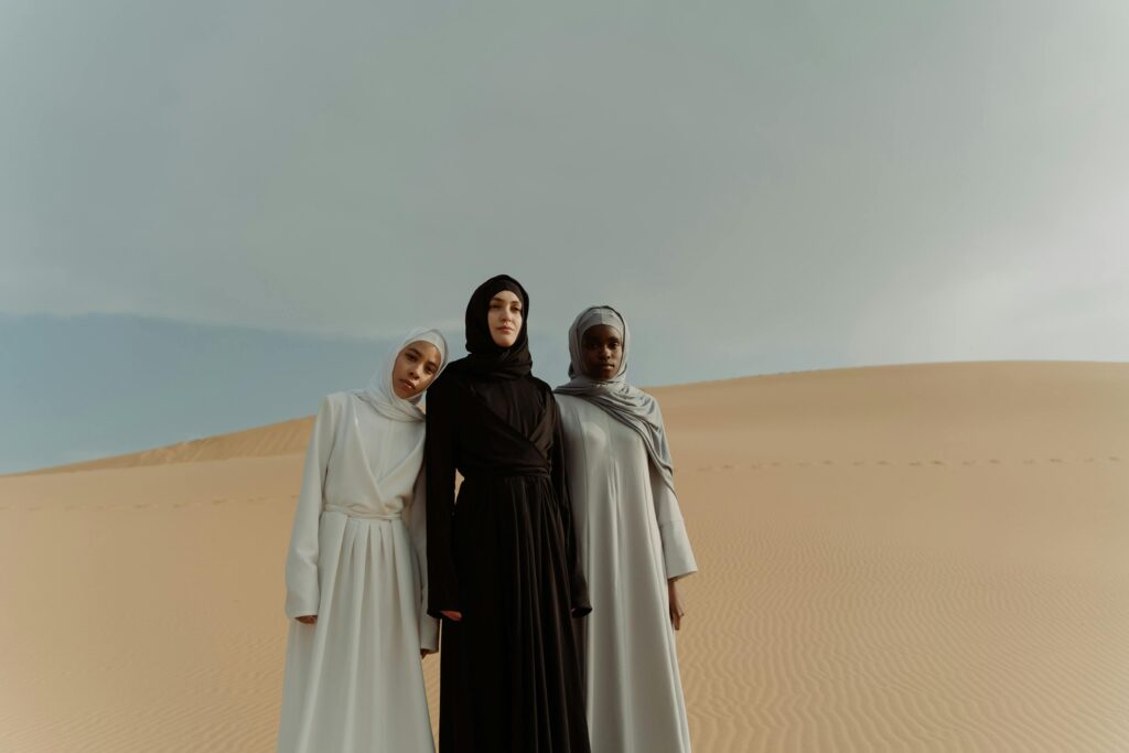 Three women wearing hijabs standing together in a serene desert setting.