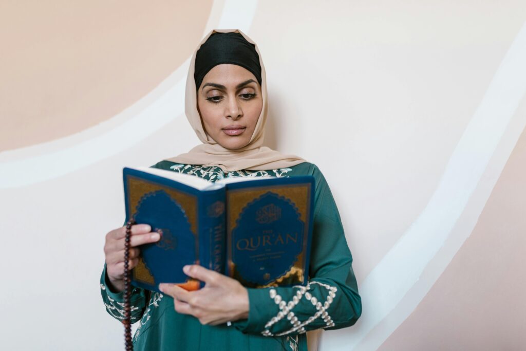 A woman in a hijab and traditional attire reading the Quran, symbolizing faith and spirituality.